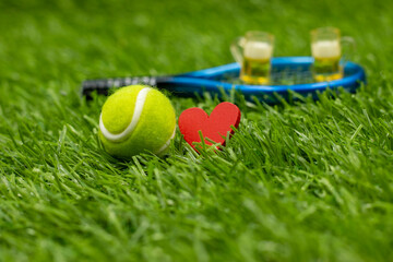 Tennis ball with glasses of beer is on green grass