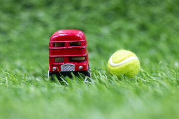 Tennis ball with double decker bus or red bus are on green grass