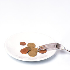 Euro cent coins on a white plate with a fork on a white background, close-up, copy space, vertical frame