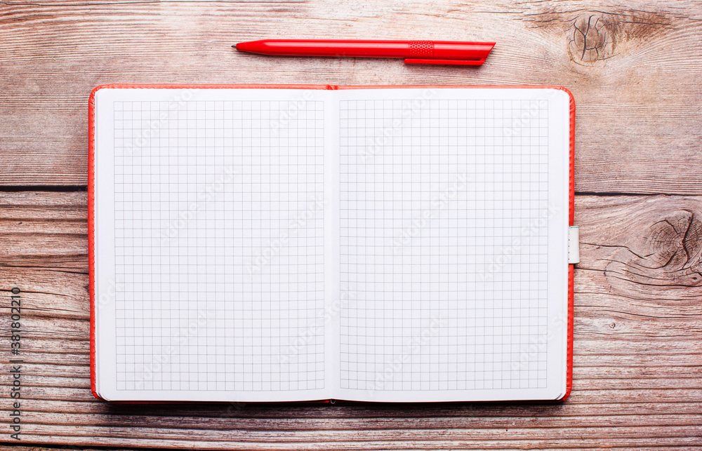 Aufkleber on a wooden table is an open notebook and a red pen.