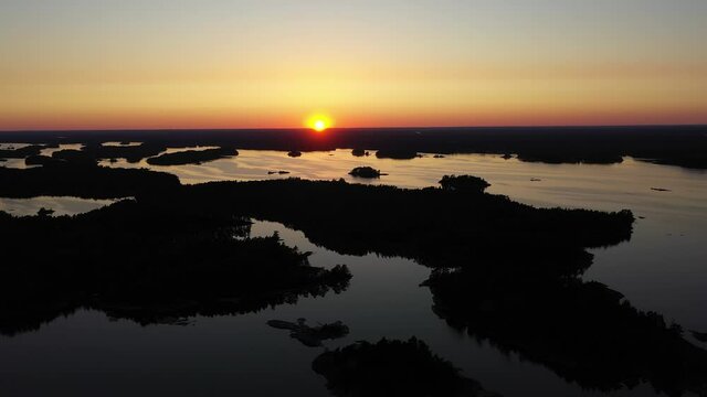 Aerial view over islands, in the Stockholm archipelago, during a colorful, summer sunset, at the Baltic sea, in Sweden - reverse, silhouette drone shot