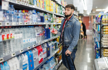 Stylish bearded guy shopping in food store, choosing water in bottles