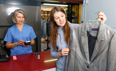 Portrait of cheerful glad beautiful female laundry customer holding clean clothes on hanger