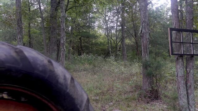Slow motion over old tractor wheel to black wooden window frame with glass panes hung in woods. Unique artistic shot.