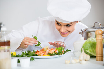 Positive female chef with plate of prepared shrimps in restaurant