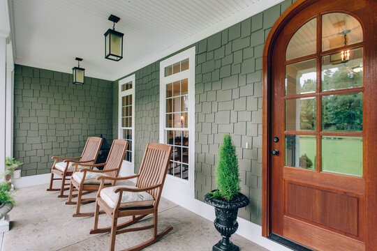 Arch Doorway Southern Covered Porch Wooden Rocking Chairs And Modern Light Fixtures With Green Bush