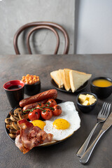 Full English breakfast  in the plate  on the restaurant table. Fried eggs, sausages, bacon, beans, mushrooms, toasts, butter, coffee, juice