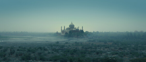 Obraz na płótnie Canvas A view of Taj Mahal from the banks of Yamuna rivers with bluish mist and clam climate 
