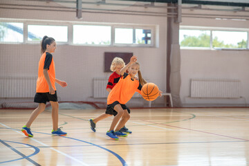 Kids in bright sportswear playing basketball together and looking involved