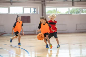 Fotobehang Kids in bright sportswear playing basketball and running after the ball © zinkevych