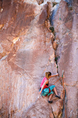 A strong woman climbs a beautiful orange rock.