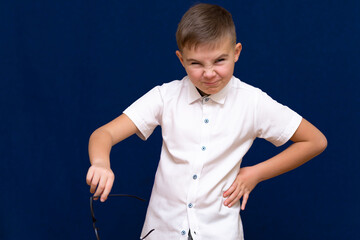 Portrait of a successful young caucasian boy.He holds and shows glasses on dark blue background.