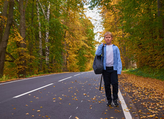 Fototapeta premium A boy with a school bag walks along the road
