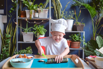 Cute happy smiling Asian little boy child wearing chef hat having fun preparing, cooking healthy Japanese food -  sushi roll at home, Fun activities for kindergarten kids concept