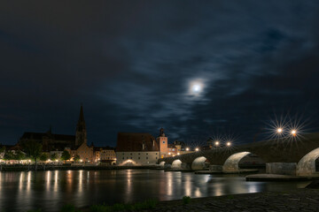 Fototapeta na wymiar Steinerne Brücke in Regensburg mit Dom und Donau und Mond bei Nacht mit Wolken