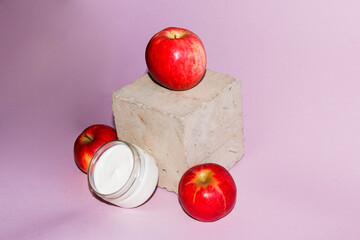 cosmetic composition with red ripe juicy apples, and an open jar with  white gentle moisturizing cream, on  pink background.