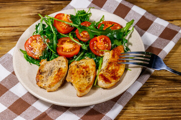 Fried chicken breast with salad of fresh arugula and cherry tomatoes on wooden table