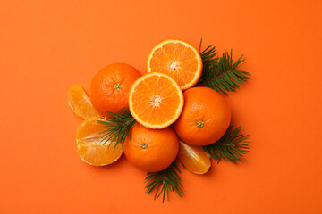 Ripe mandarins and pine branches on orange background, top view