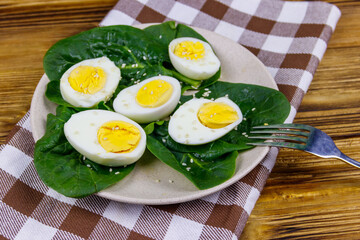 Boiled eggs with fresh spinach leaves and sesame seeds on wooden table
