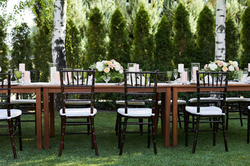 Fototapeta na wymiar chairs and dinner tables with white cloth, served with porcelain and green glasses. Georgeous wedding or event party table decorated with flowers on a green lawn
