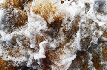 Background of white sea foam close up mixed with sand during sea surf