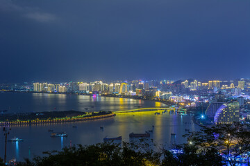 Fototapeta premium Night view of Sanya city with bright multi-colored illumination buildings, structures, roads, sidewalks, poles, bridges.