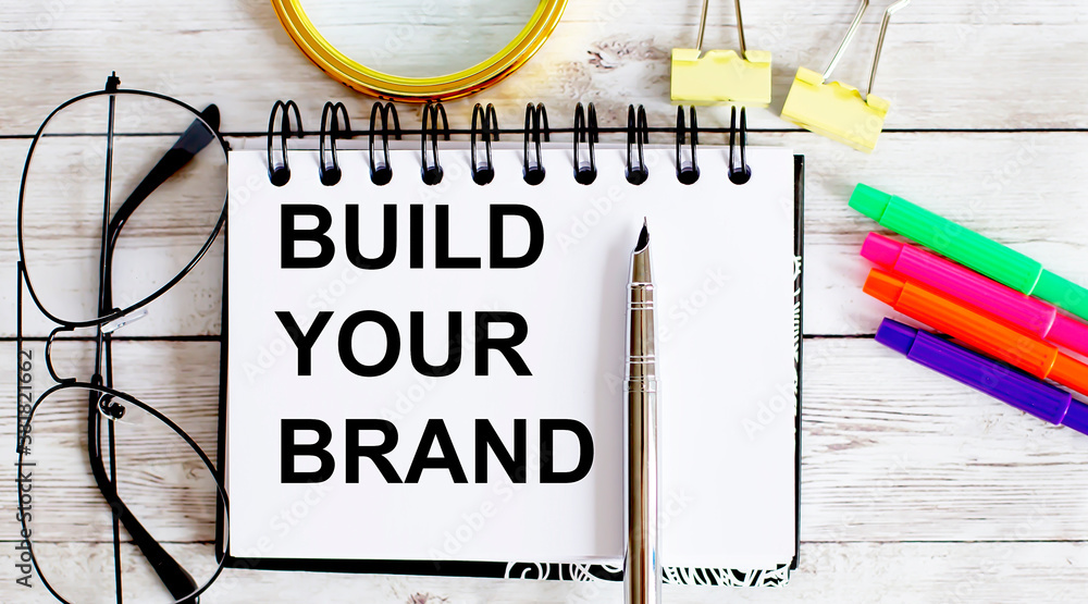 Poster build your brand written in a notebook on the white background with office tools