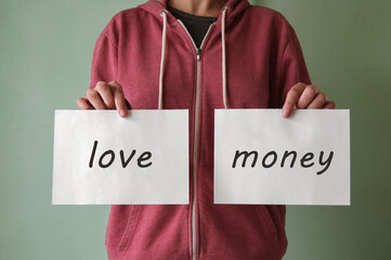 A young man holds a piece of paper with the words LOVE and MONEY.