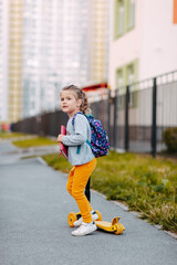Little girl goes to school for the first time. Little student with purple backpack and pink notebook going to school with yeallow scooter.