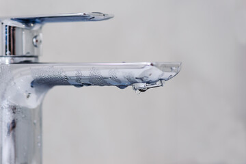 Faucet with a drop of water on a gray background. Hot water shutdown concept.