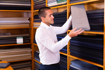 Male seller demonstrates various fabrics in store. High quality photo