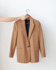A hand holds a classic beige jacket on a wooden hanger. Dress code in the office