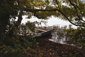 
Fishing boat on the lake standing on the shore under the trees. And around the autumn forest