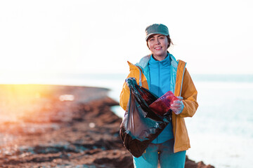 A young Caucasian woman in a jacket collects garbage and puts it in a plastic bag. Light. In the...