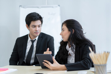 Asian and caucasian ethnicity partnership businesspeople discuss a business plan together by using touchscreen tablet in the meeting room in office. Co-worker colleague and teamwork concept.