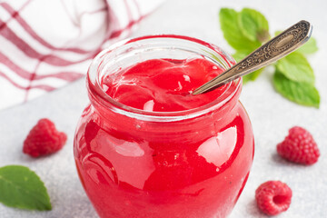 Homemade raspberry jam in a glass jar and fresh raspberries with mint on a grey concrete background. Copy space