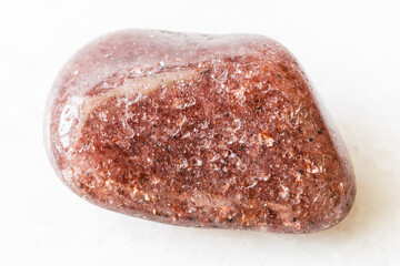 closeup of sample of natural mineral from geological collection - tumbled red aventurine gem stone on white marble background from Canada