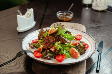 warm chicken liver salad with figs is served on a white plate with a sauce of French mustard and honey. Close up