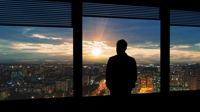 The man stands near the window on the night urban background. time lapse