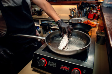 chef is frying mullet in a frying pan on an electric stove. Cooking fish dishes in the cafe