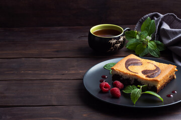 A piece of double-layer cake on a plate of chocolate brownies and curd cheesecake with raspberries. Dark background copy space