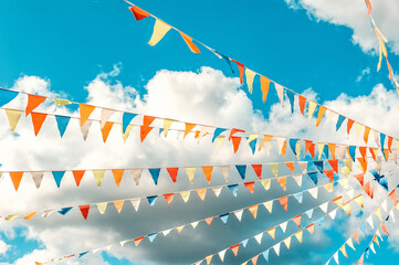 Colorful bright triangular Bunting flags on a blue sky background with white clouds. The concept of...