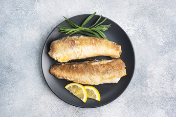 Fried fish hake Pollock and slices of fresh lemon. grey concrete background. Copy space.