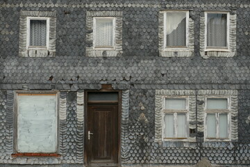 Fototapeta na wymiar Alte Schindelfassade eines verlassenen Hauses mit sieben Fenstern und Türe