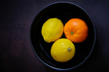 Lemon and orange on black bowl in dark background