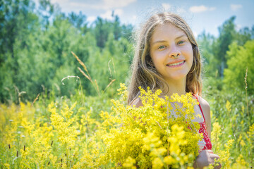 Naklejka na ściany i meble In summer, on a bright sunny day, a girl stands in a bright red dress on a blooming field.