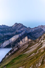 Colorful sunrise on the steep ridge of the majestic  Schaefler peak in the Alpstein mountain range Appenzell, Switzerland with the fog covering the Seealpsee valley