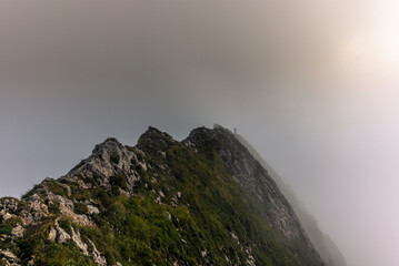 Fog and clouds enveloping a clmber on the steep ridge of the majestic Schaefler peak in the Alpstein mountain range in Appenzell