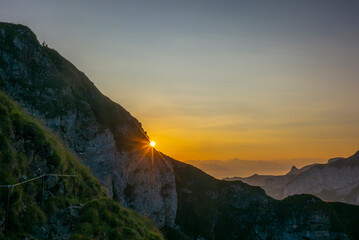 Hikers in the distance observing the colorful sunrise on the steep ridge of the majestic Schaefler peak in the Alpstein mountain range Appenzell, Switzerland