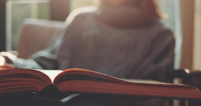Woman's Hand Turning Pages of a Book, Cozy Morning. SLOW MOTION, CLOSE UP. Unrecognizable Girl reading a book and holding fingers along the lines. Cinematic light, comfort of a home. Lens Flare.
